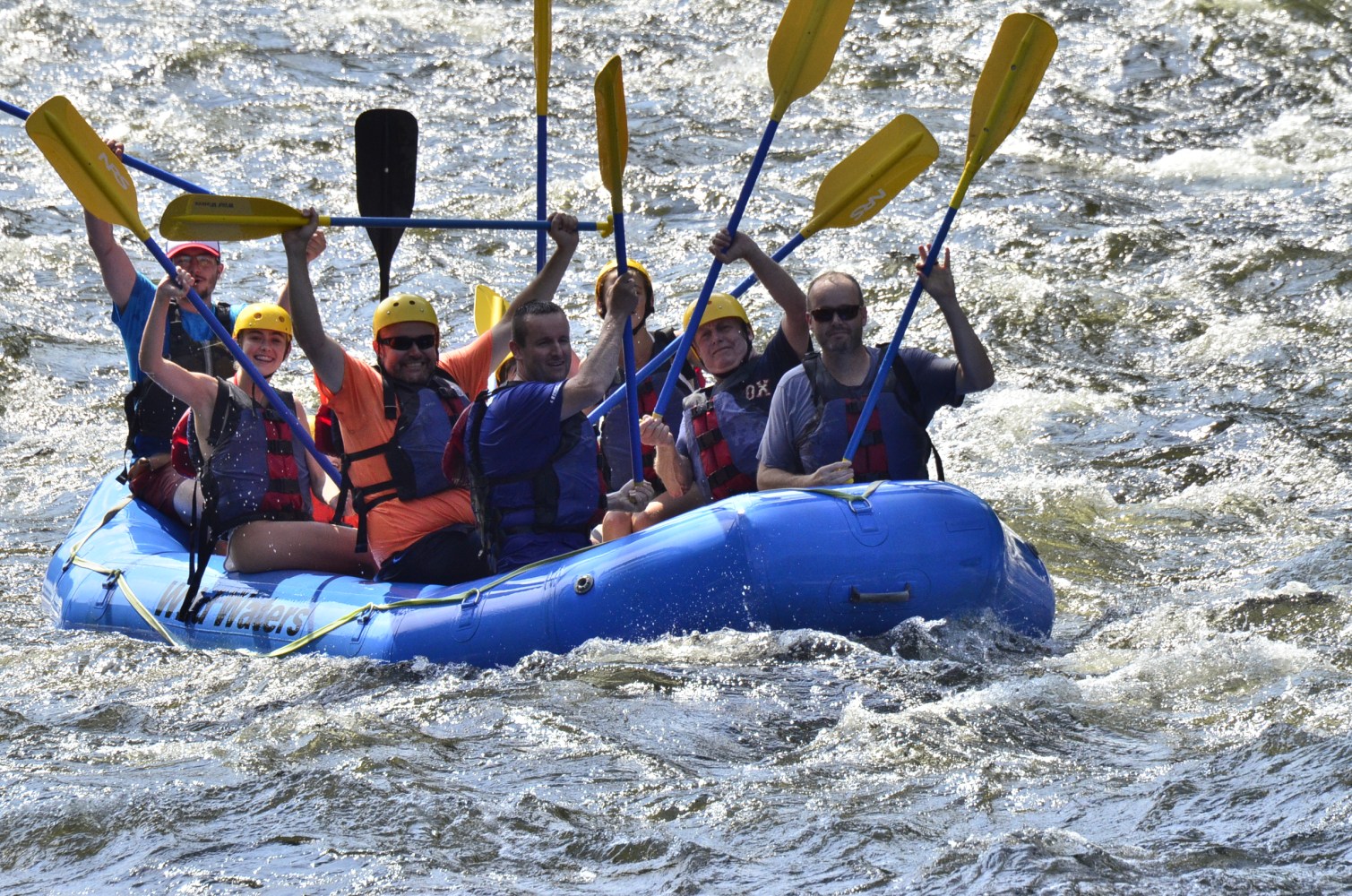 Group rafting on a river in a blue inflatable boat, wearing helmets and life jackets.