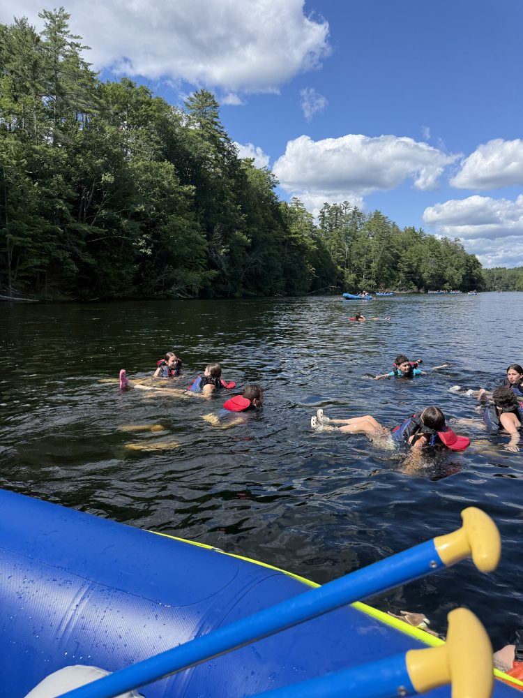 People swimming with floats near a paddleboard on a lake.